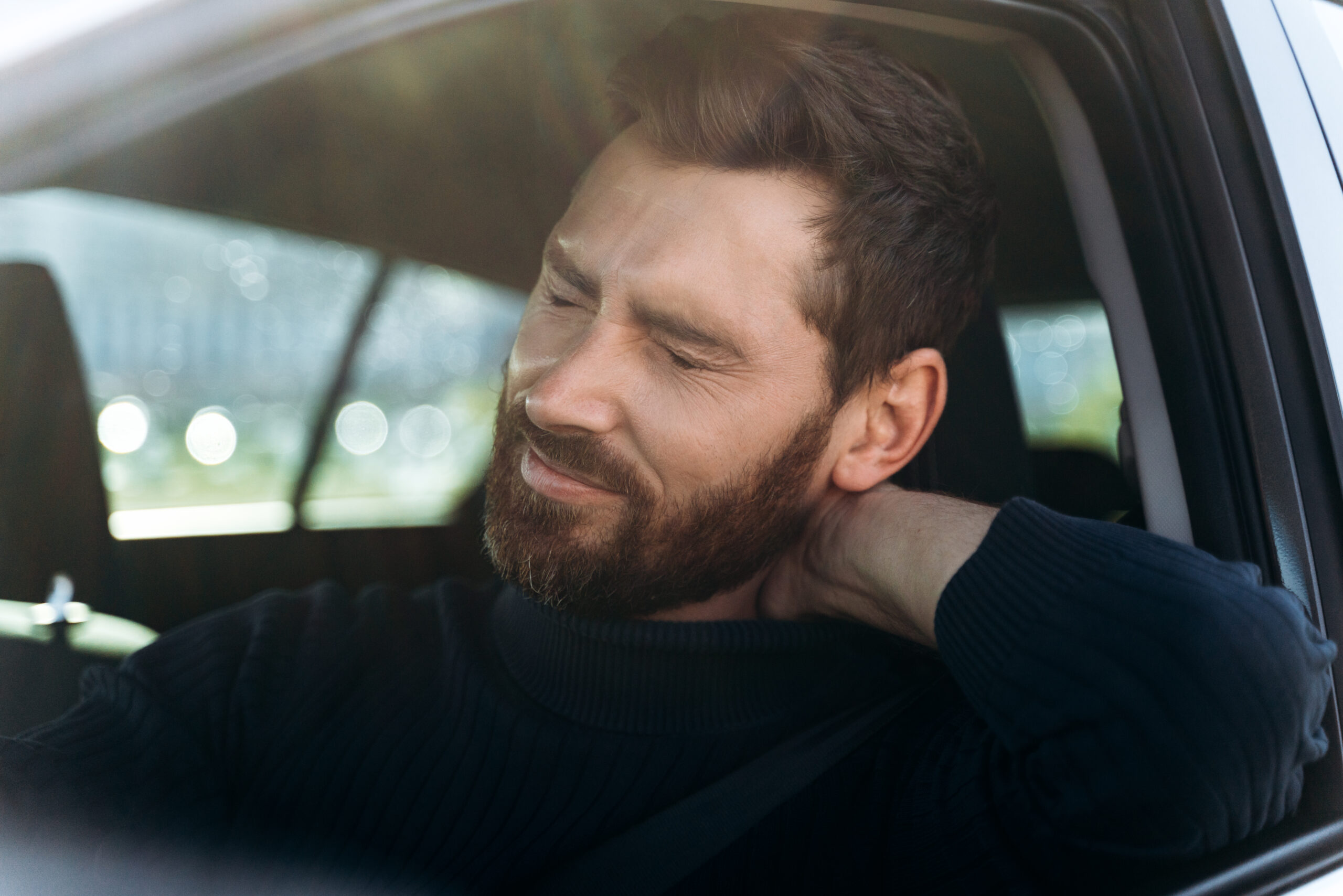 Man in car with hand behind head looking concerned or stressed - could benefit from Relational Life Therapy.